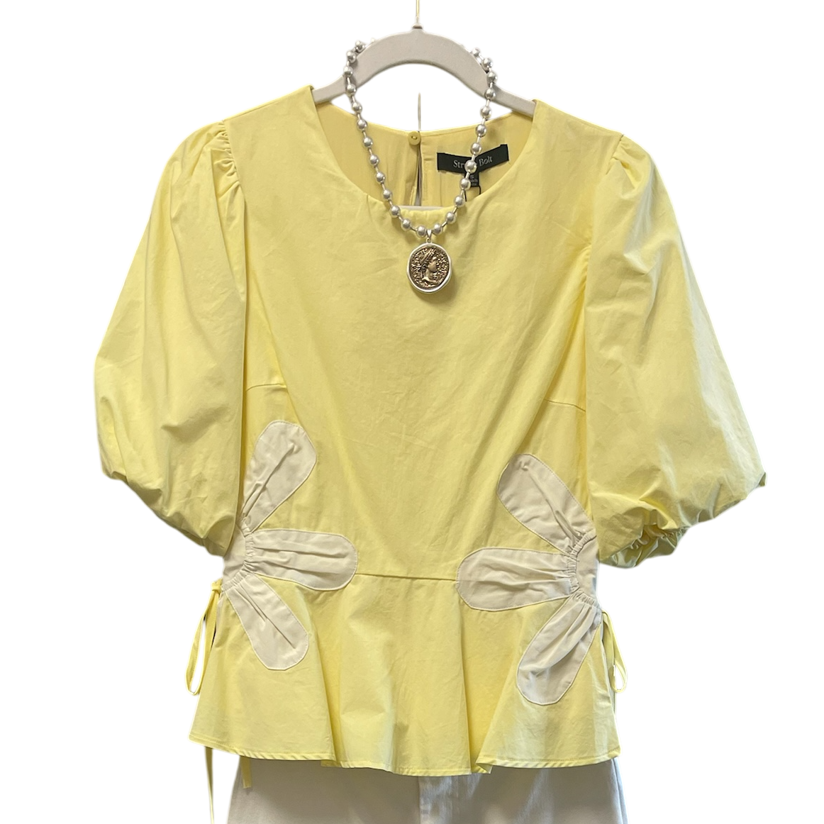 Yellow blouse with bow details on a hanger against a white background